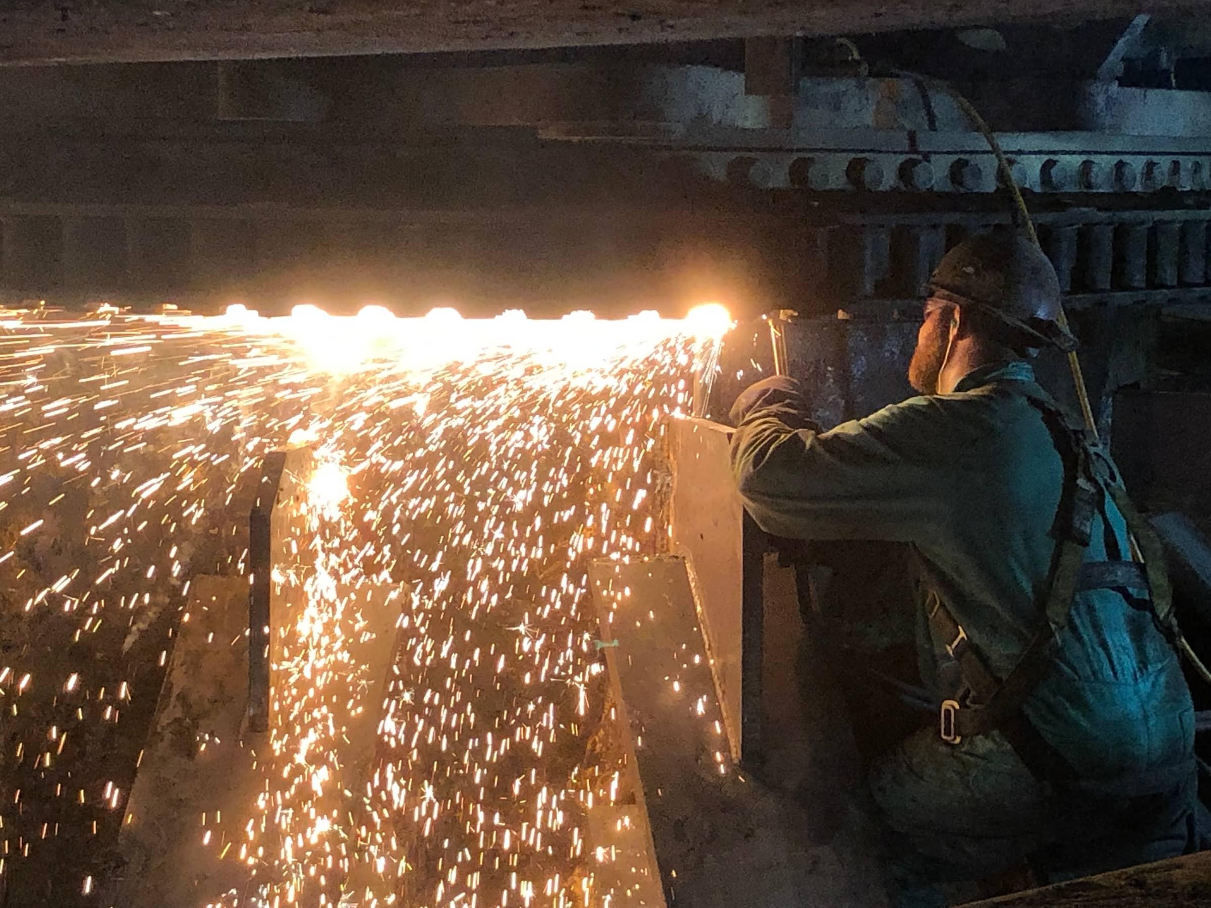 Torch cutting throwing sparks under a structure