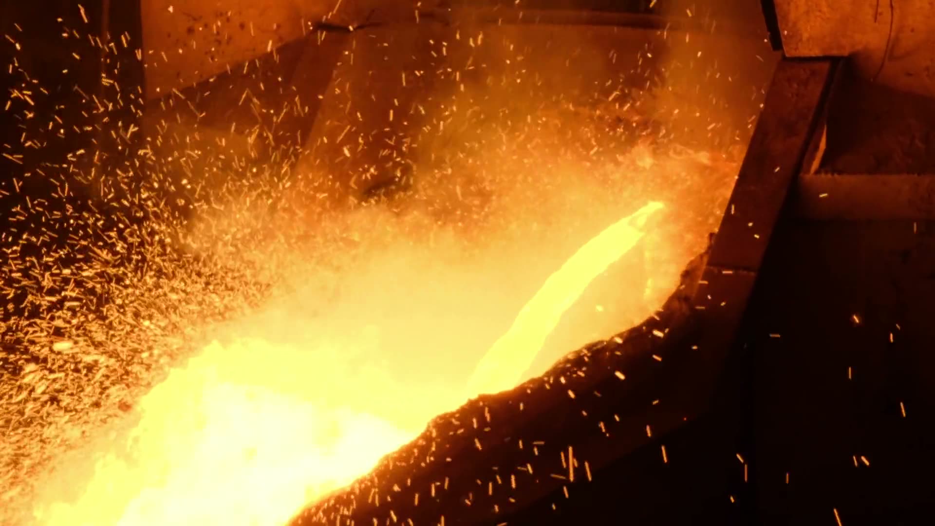 A furnace tapping: molten steel running down a trough in a shower of sparks.